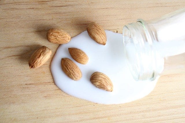 Almond milk spilling onto a wooden background with whole almonds