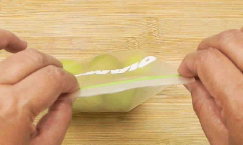 A woman's hands sealing up a freezer bag of whole limes on a wooden chopping board background