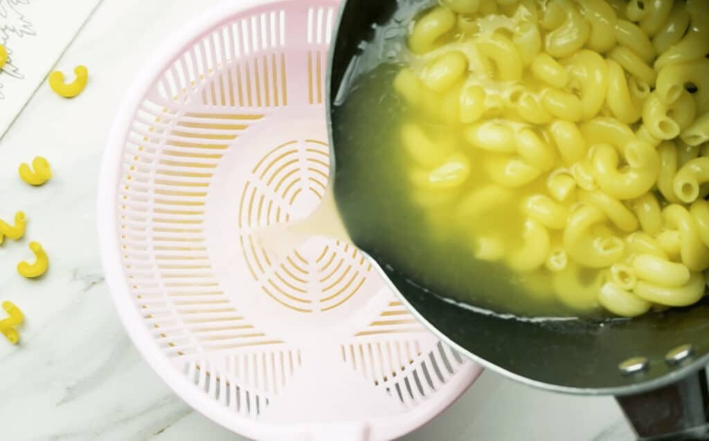 Cooked macaroni elbow pasta in a pot of water being drained into a white colander