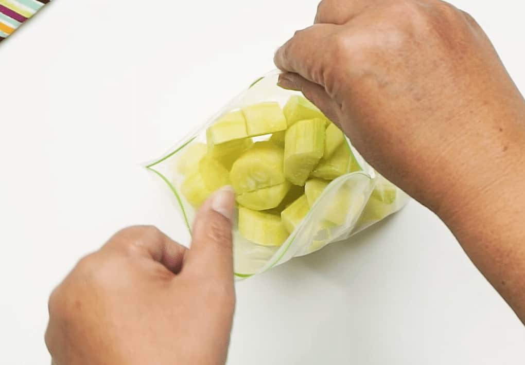 Frozen courgette pieces in an open freezer bag being held by a woman's hands 
