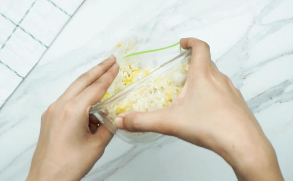 A woman's hands tipping a glass bowl of egg fried rice into a freezer bag