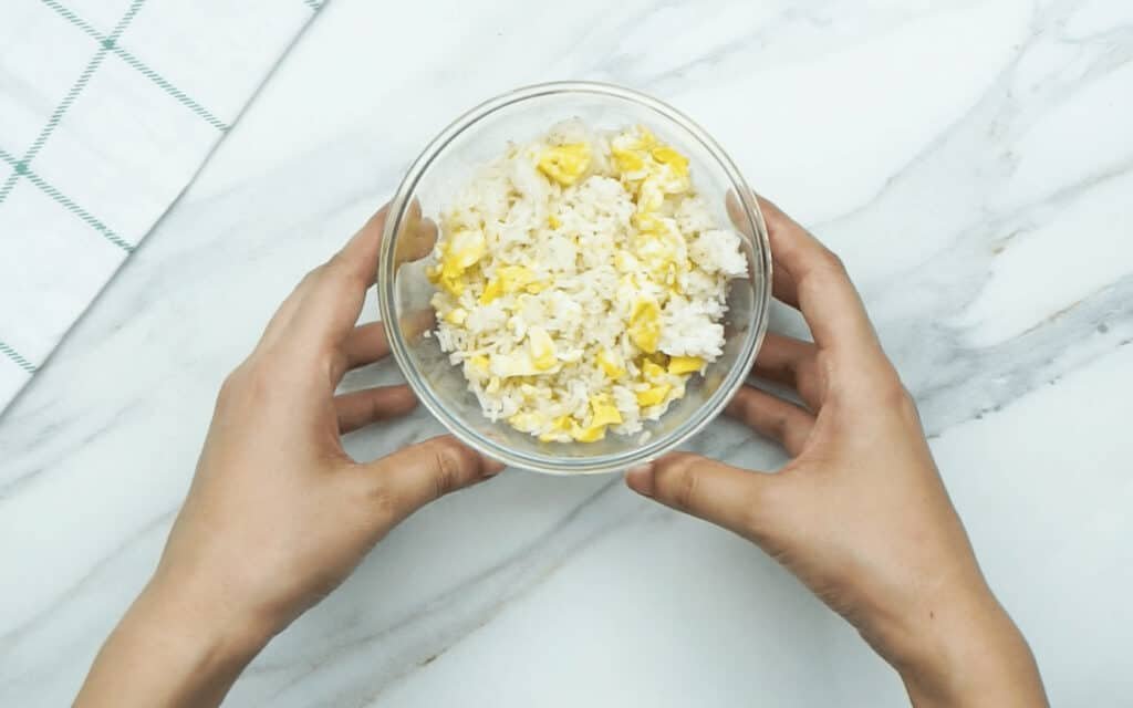 Cooked egg fried rice in a glass dish being held by a woman's hands