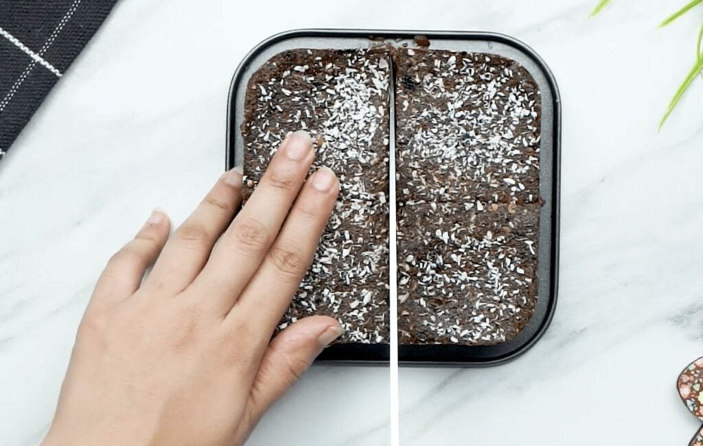 A woman's hand slicing down the centre of a freshly baked brownie slab preparing to cut the brownie into portions