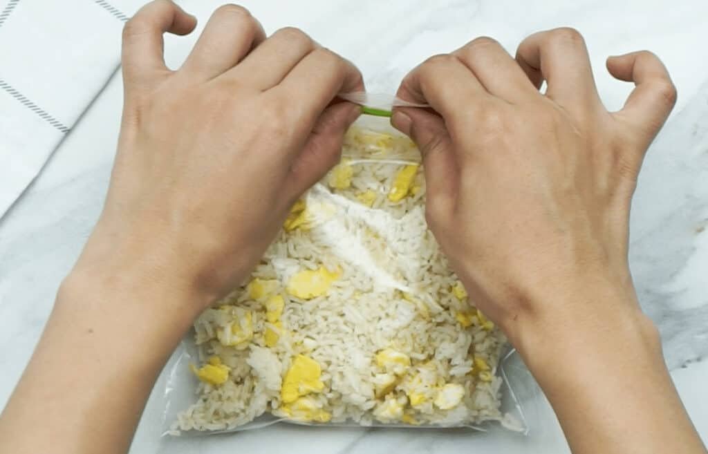 A woman's hands sealing up a freezer bag containing egg fried rice